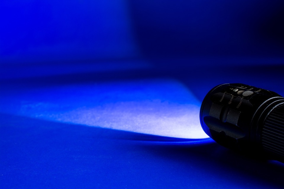 Taschenlampe in einem dunklen Raum erleuchtet einen kegelförmigen Bereich auf einer Tischplatte.